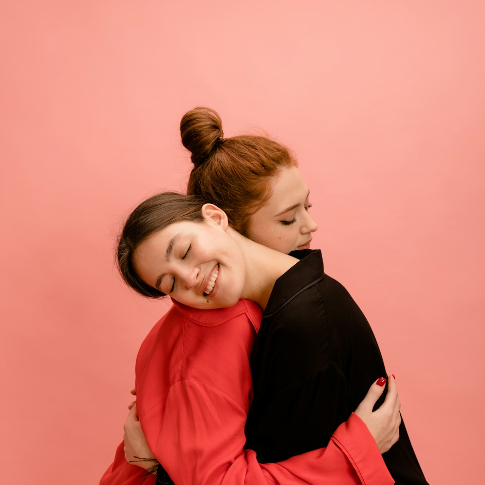 Two women hugging and laughing on a pink backdrop
